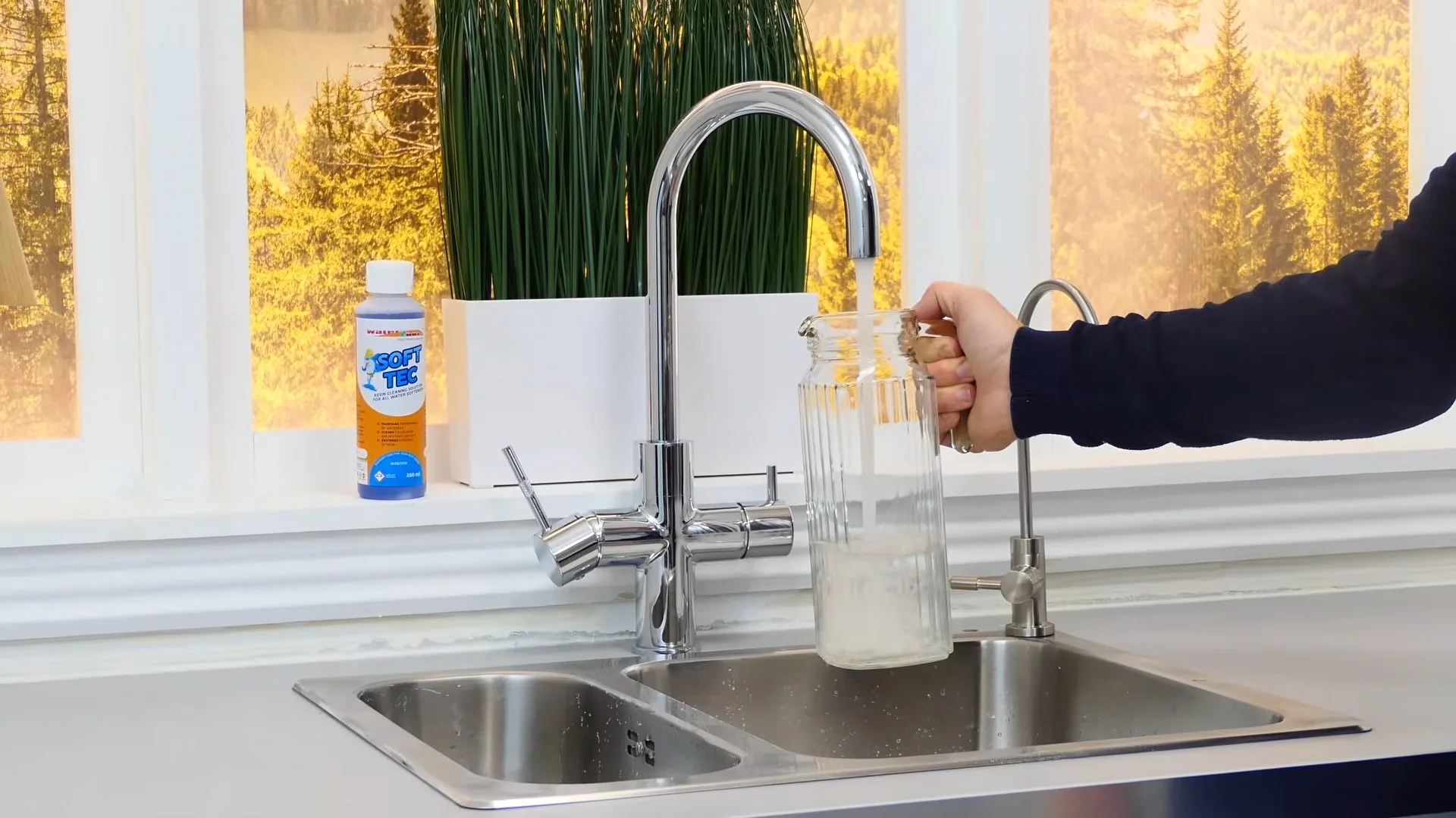 Chrome faucet filling a glass jar at a double sink under a bright kitchen window