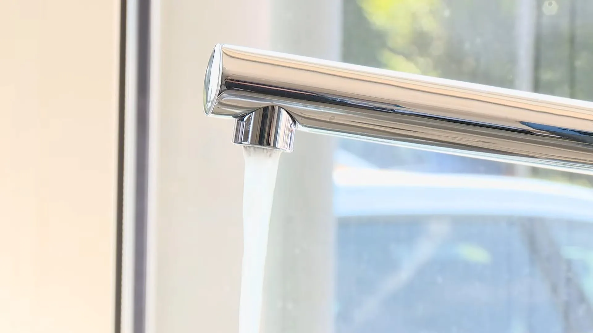 Chrome faucet spout with a clear stream of water beside a bright window