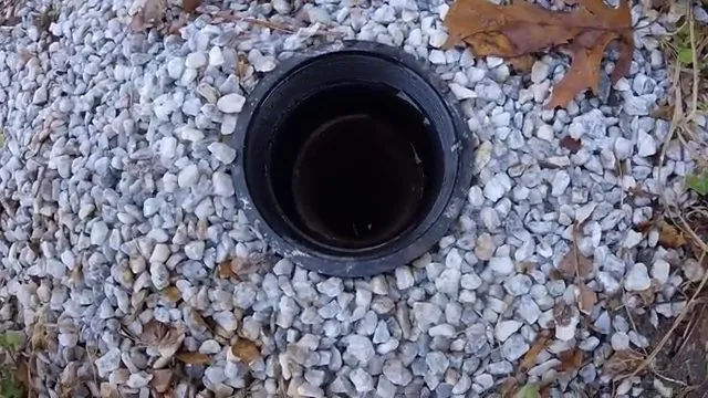 Black cleanout pipe opening set in white gravel with leaves around it