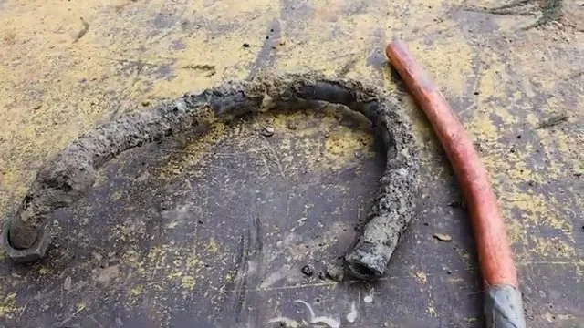 Crusted corroded pipe lying in a curve beside a clean length of red PEX tubing on a shop floor