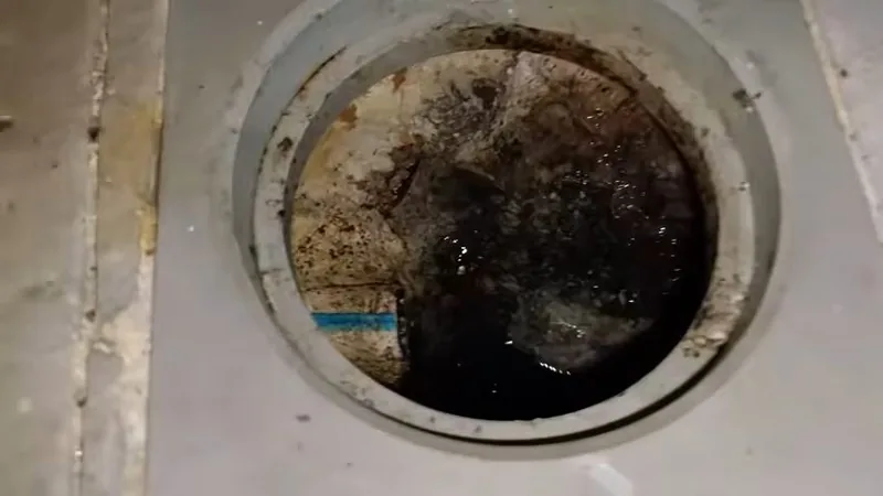 Looking down into a round floor drain opening with dark standing water and grime around the rim