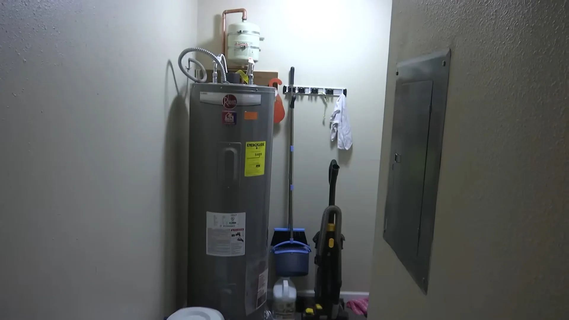 Electric tank water heater standing in a utility room next to a breaker panel