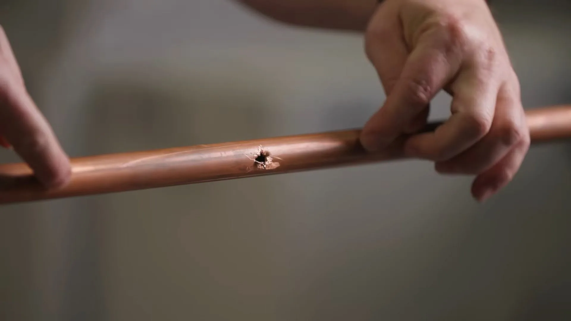 Two hands holding a length of copper pipe with a small split hole near the middle