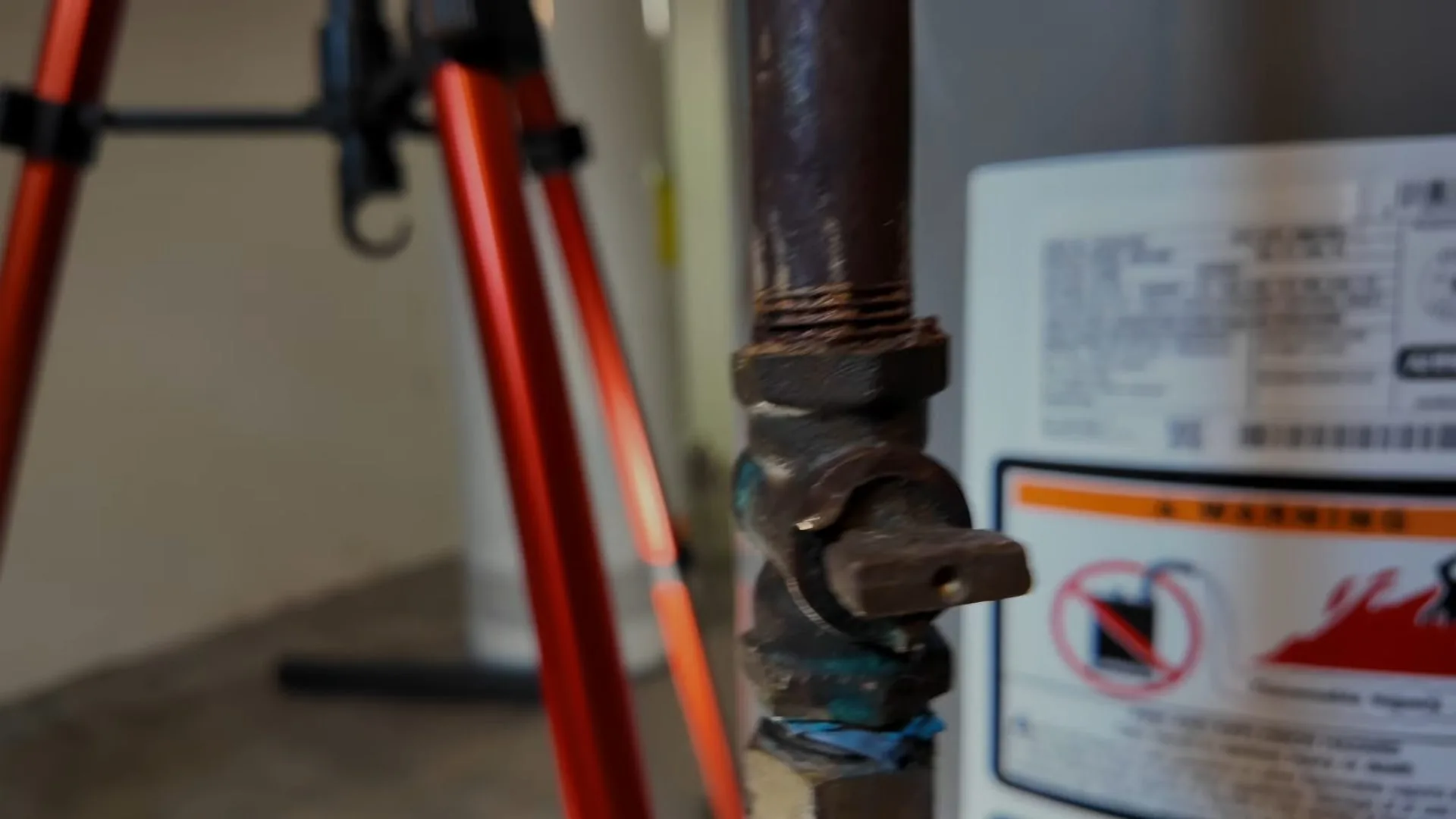 Black iron gas shutoff valve with a yellow handle beside a water heater warning label