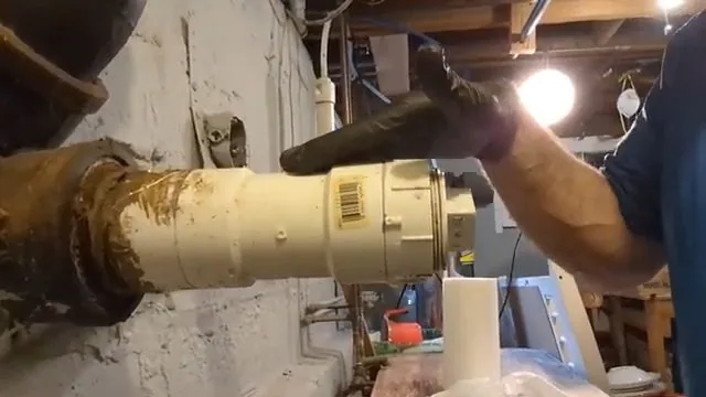 Gloved hand reaching toward a cream-colored capped cleanout on a pipe in a basement