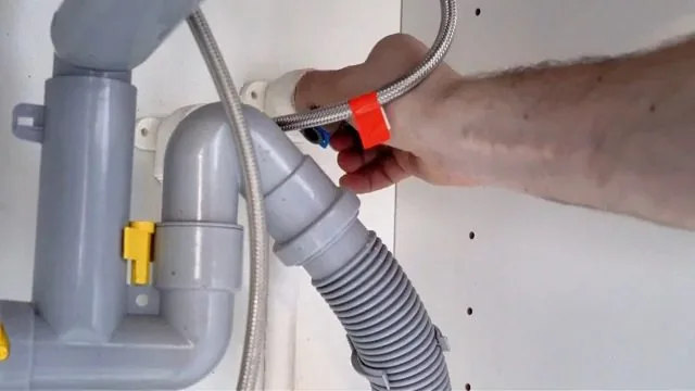 Hand holding a braided supply line next to a gray drain trap and flexible hose under a sink