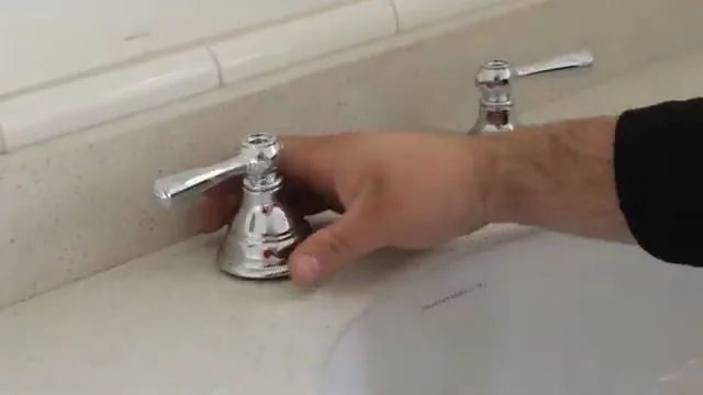 Hand on a chrome two-handle bathroom faucet set into a white countertop