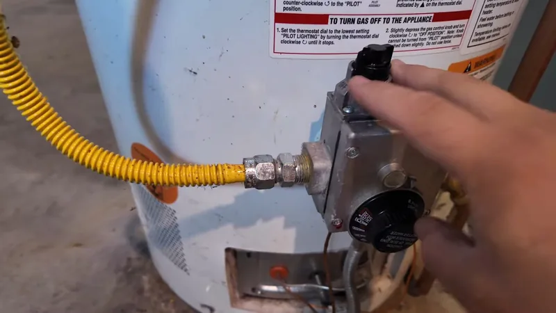 Hand on the black gas control knob of a gas water heater with a yellow gas line attached