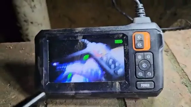 Handheld inspection camera with an orange bumper showing the inside of a pipe on its screen