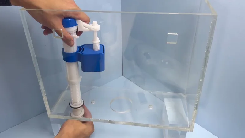 Two hands holding a blue and white fill valve inside a clear acrylic toilet tank