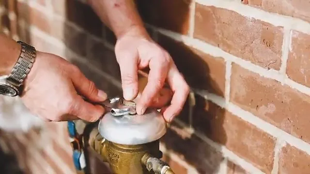 Hands turning a brass valve at a water meter mounted on a brick wall