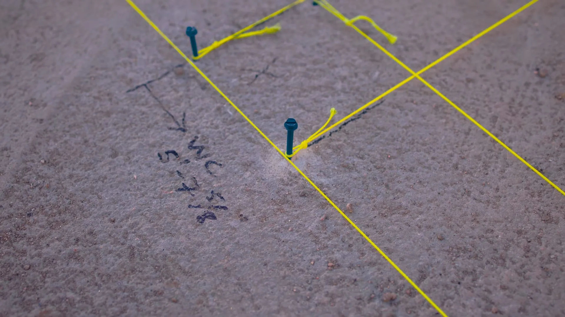 Carpet with yellow string lines, blue pins and a handwritten arrow marking a location over a slab
