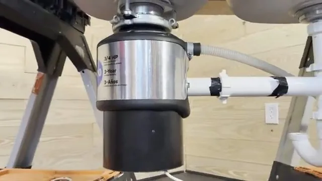 Stainless garbage disposal mounted under a double sink with a white drain pipe running to the side