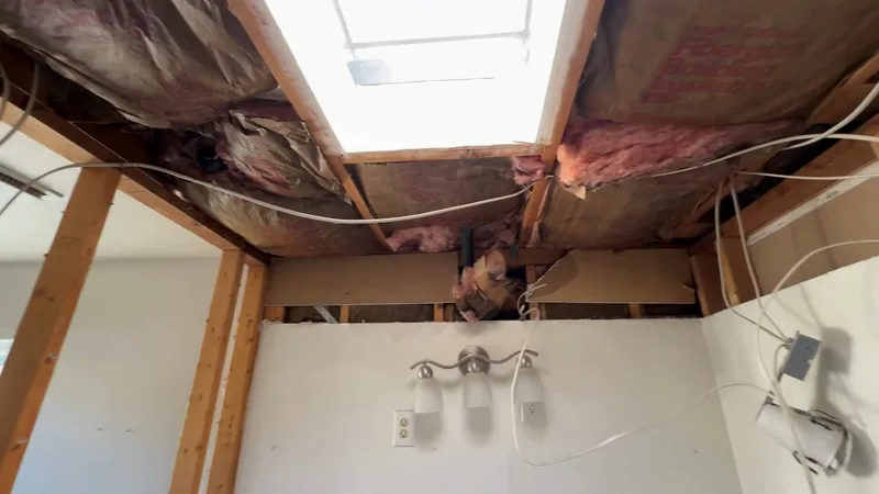 Room with the ceiling opened to bare joists and pink insulation, a light fixture hanging below
