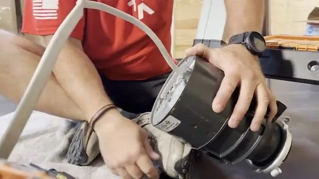 Person in a red shirt holding a black garbage disposal unit on their lap with its cord trailing