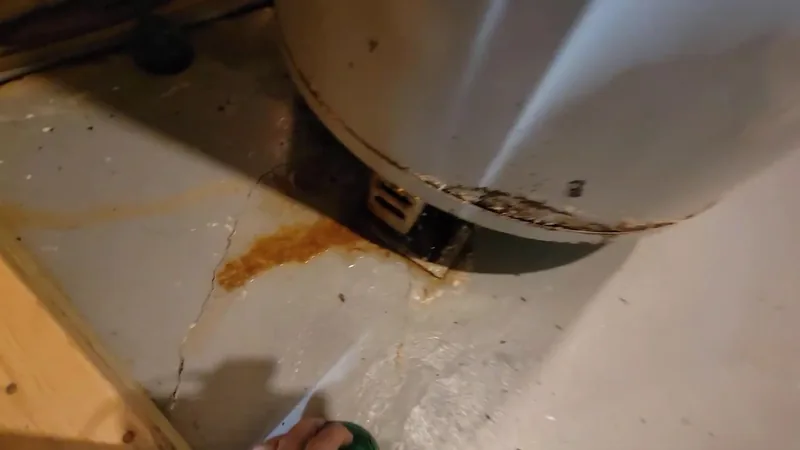Orange rust stain and a crack in the floor pan beneath the base of a water heater tank
