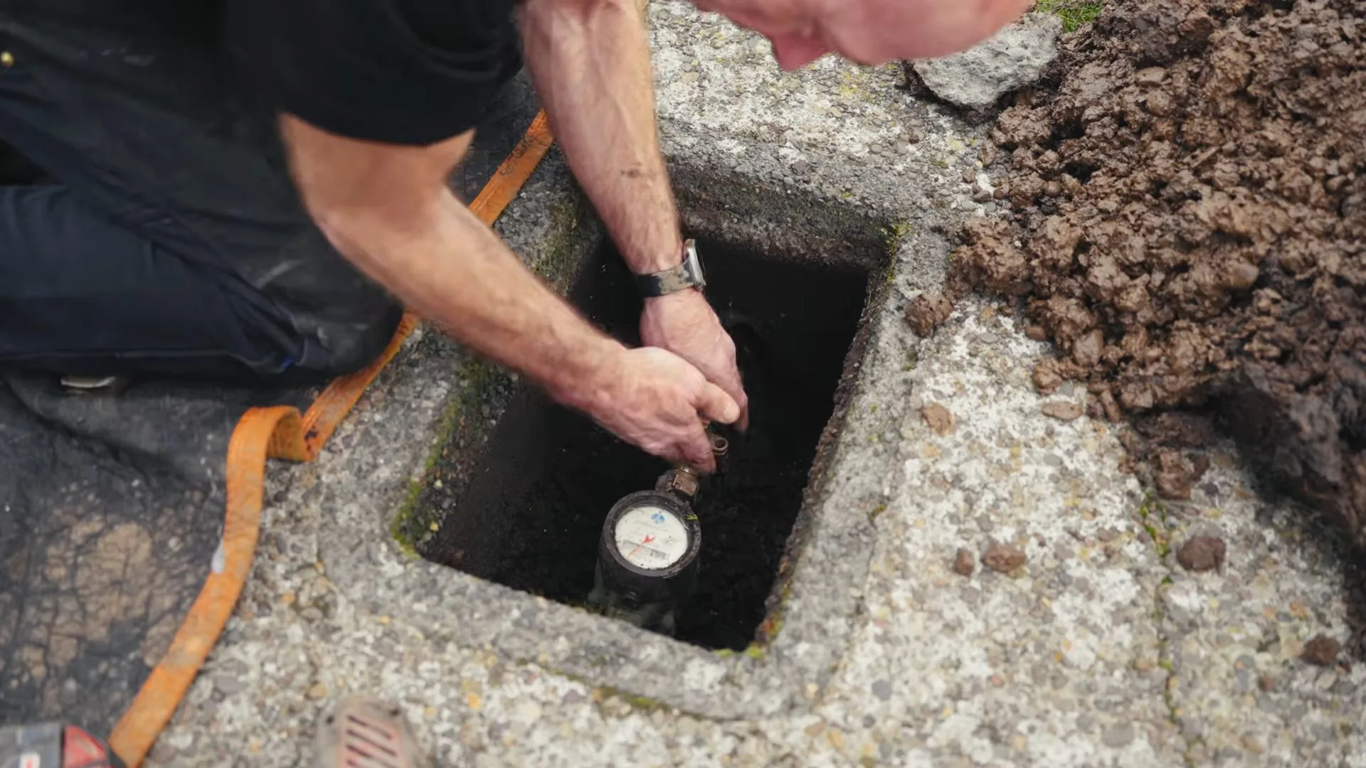 Technician kneeling at an open meter box in a concrete pad and reaching toward the water meter