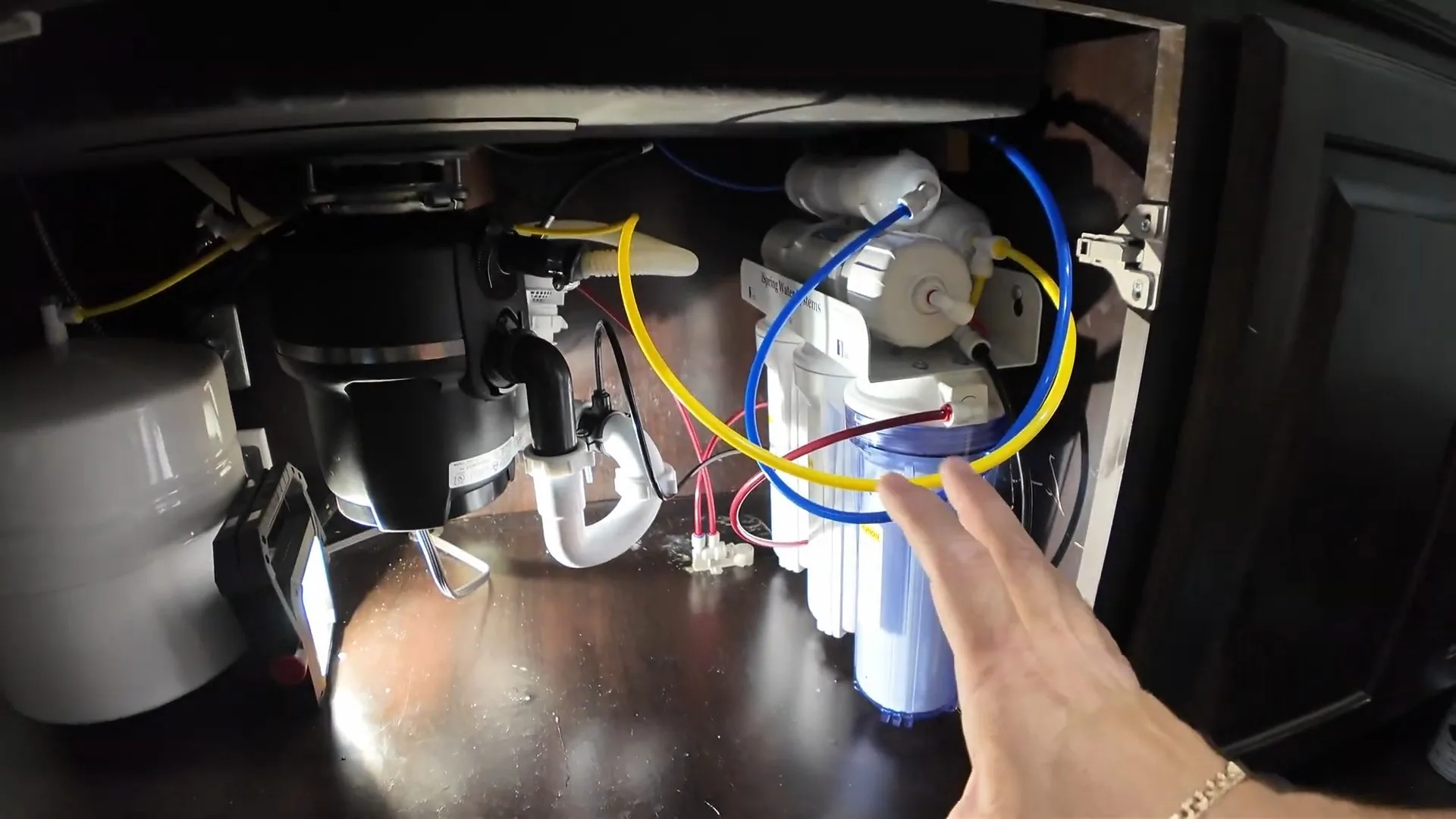 Open under-sink cabinet with a garbage disposal on the left and a multi-stage water filter system with colored tubing