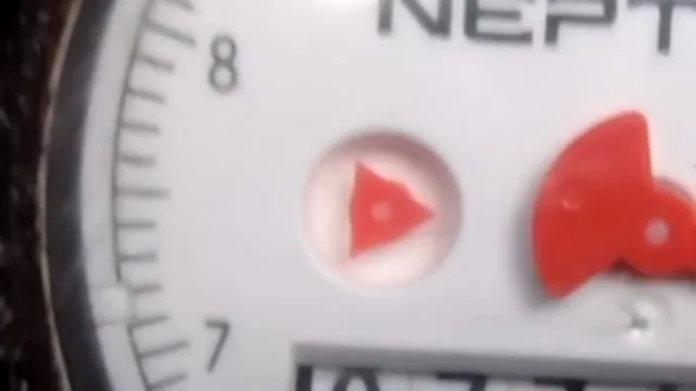 Close view of a water meter dial with a red triangle low-flow indicator and a red sweep hand