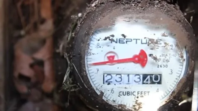 Water meter dial with a red sweep hand and a cubic-feet readout, dirt around the edge of the glass