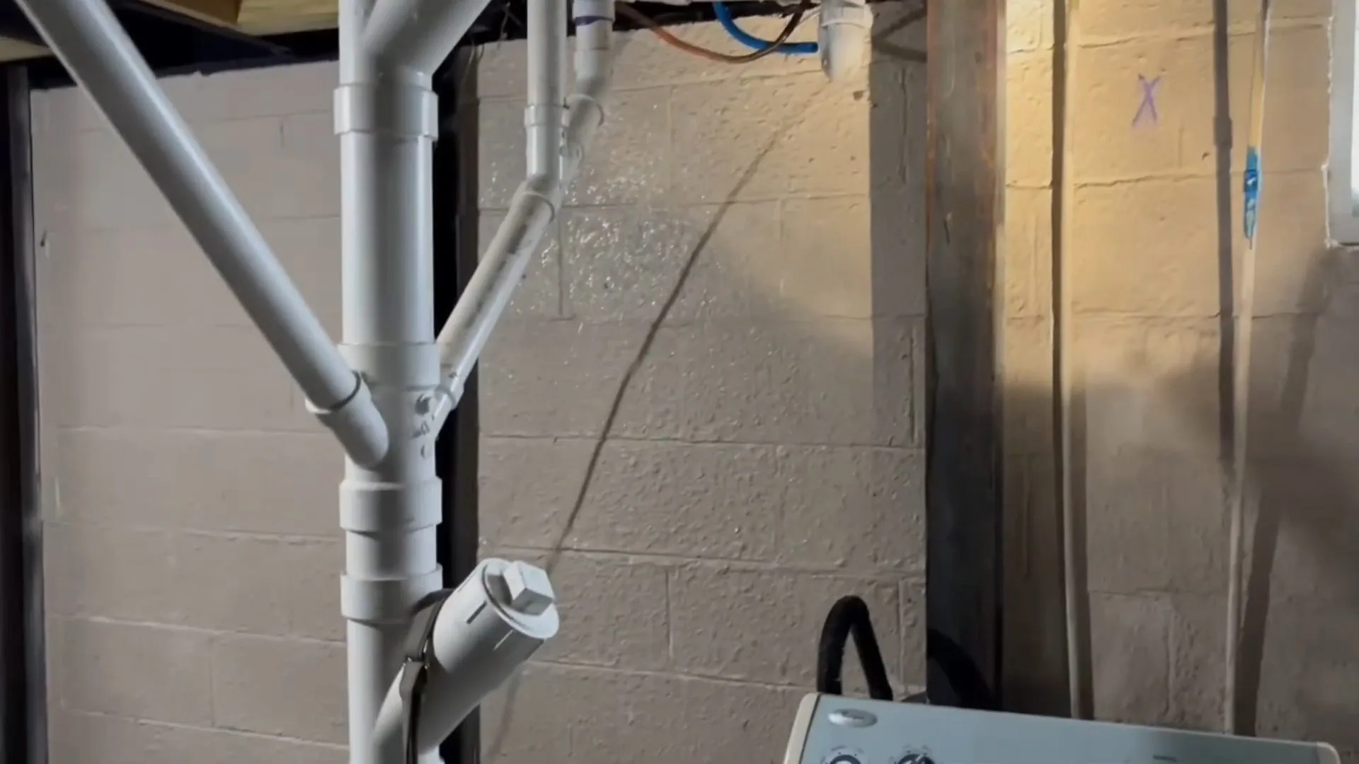 White PVC drain stack with a capped cleanout rising along a painted block basement wall