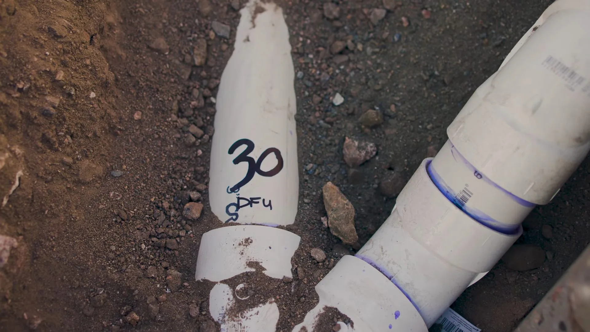 White PVC pipe fittings marked with a 30 DFU note lying in dirt